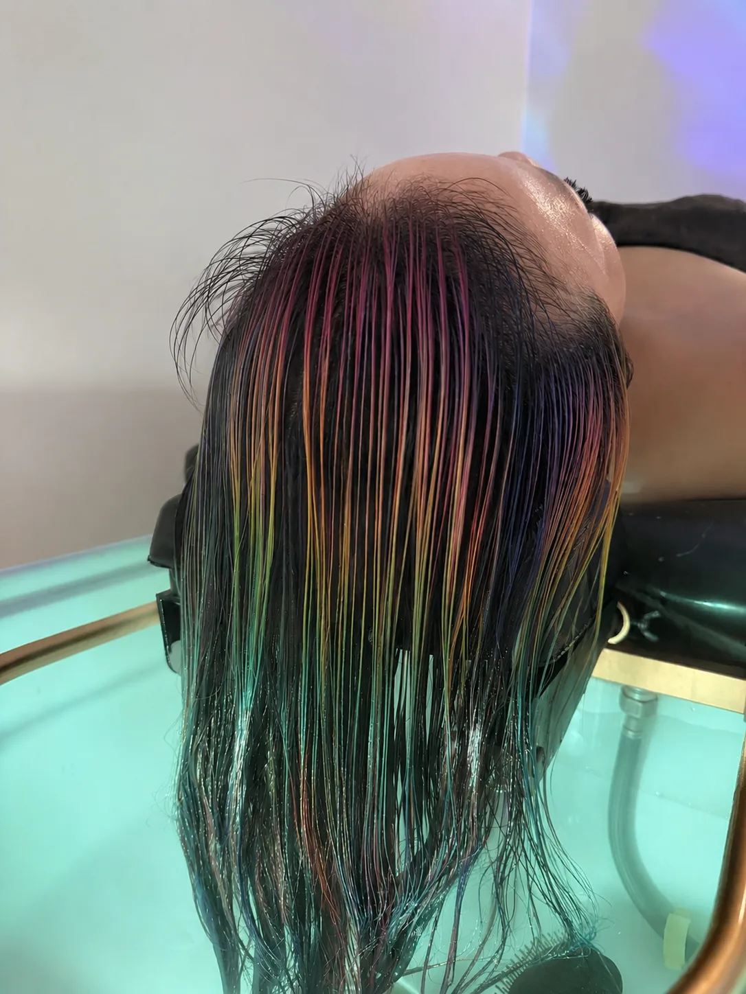 Colour-gloss treatment draped over the green-lit glass basin, the back of the head, no face visible