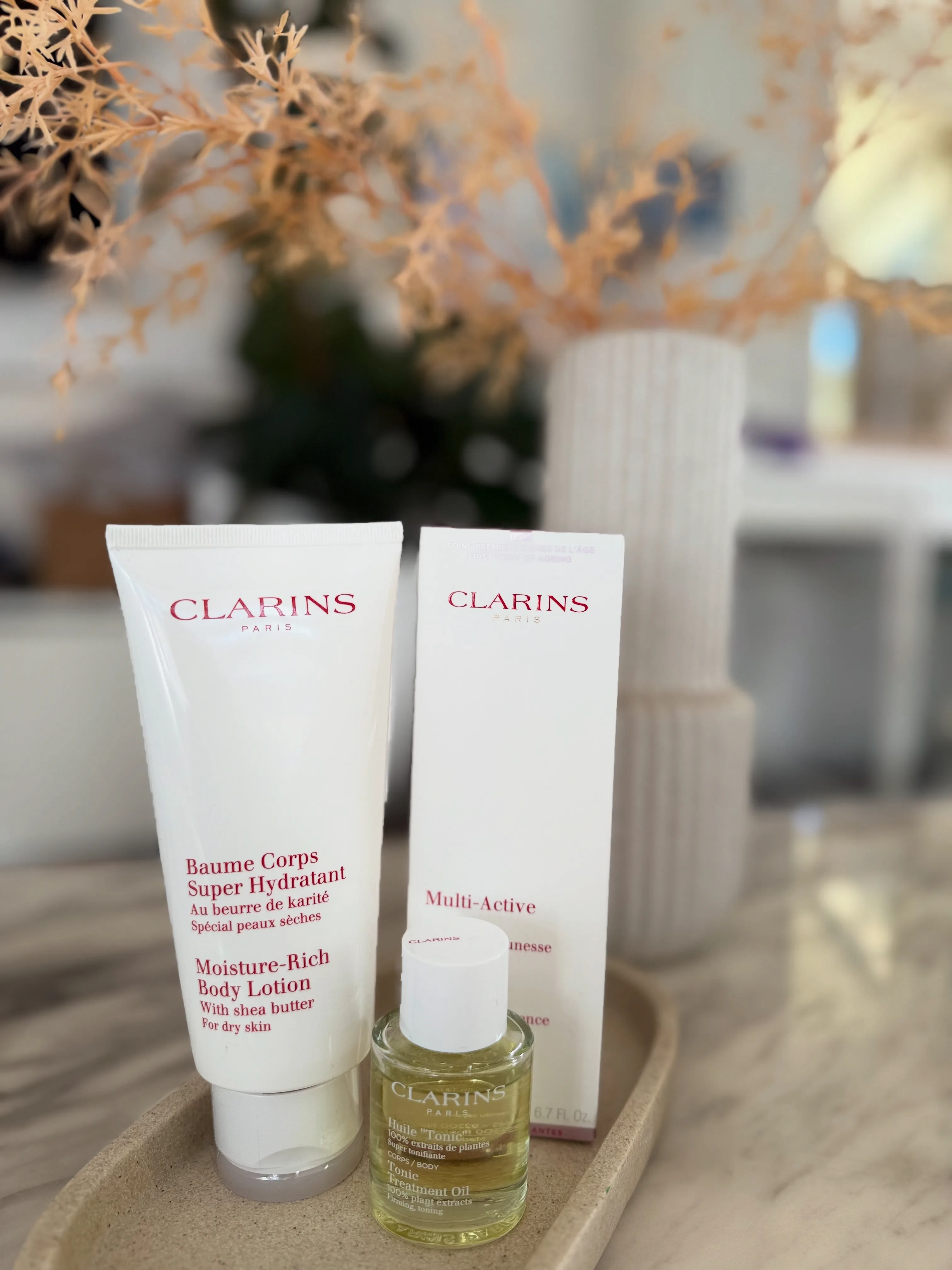Gentle professional skincare — Clarins bottles styled on a stone tray with dried florals