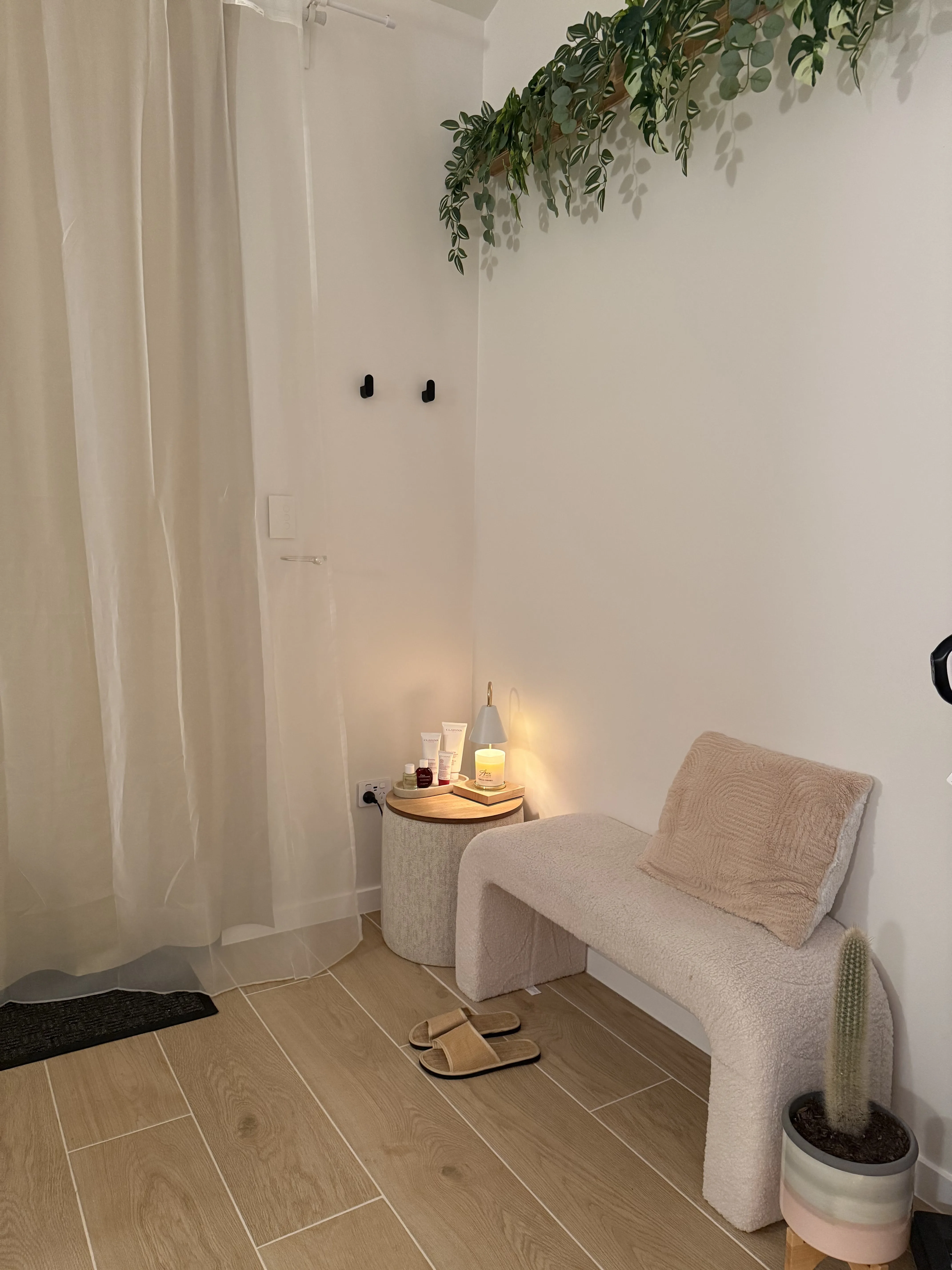 Serene entry corner — bouclé bench, trailing greenery, candle and Clarins on the side table