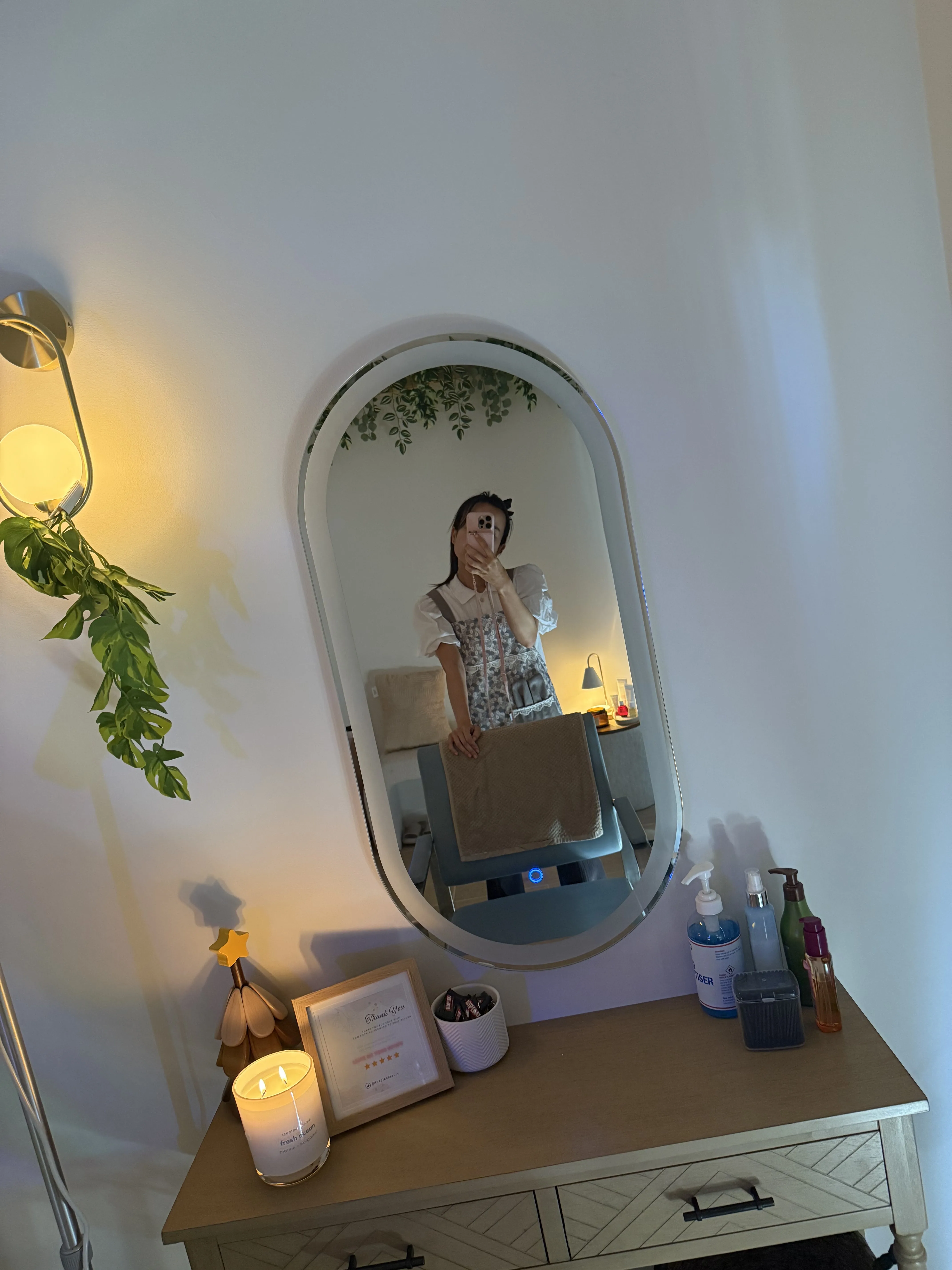 Vanity area with the oval LED mirror, a framed thank-you card, sanitiser and product shelf