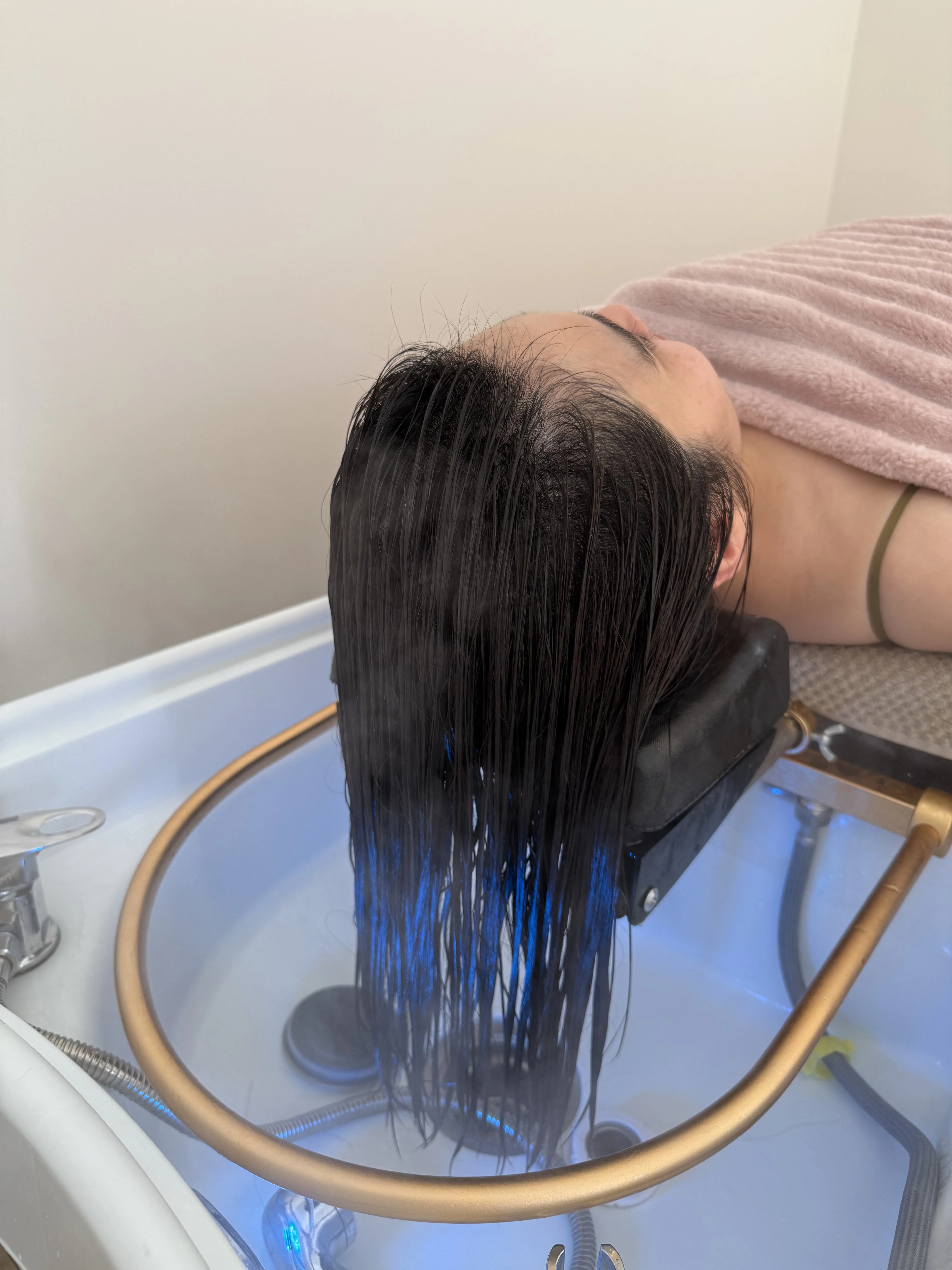 The water-halo ritual — long dark hair fanned out over the gold halo ring into the basin, client on a blush towel